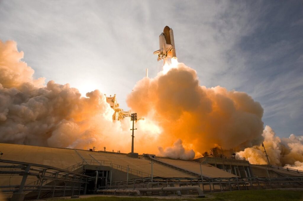 Dramatic view of a space shuttle launching, surrounded by smoke and fire.